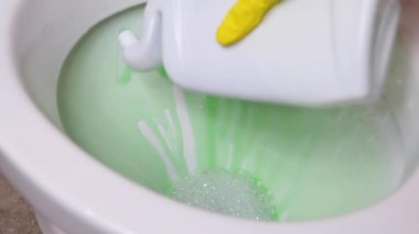 Kadın klozeti çamaşır deterjanıyla temizleyip dezenfekte ediyor.