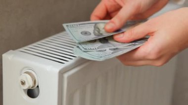 Bir radyatörün arka planında kadın ellerine bırakılmış dolar banknotları..