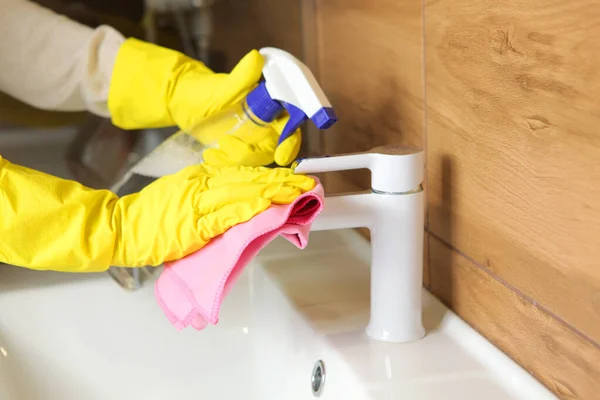 Mulher limpa a pia e torneira no banheiro, limpeza e desinfecção — Fotografia de Stock