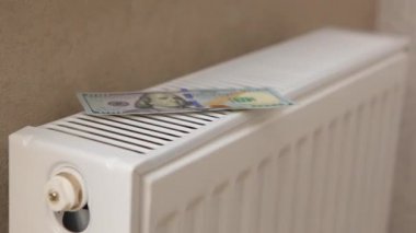 Bir radyatörün arka planında kadın ellerine bırakılmış dolar banknotları..