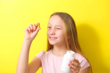 Genç bir kız elinde renkli bir arka planda omega 3 kapsülü tutuyor.. 