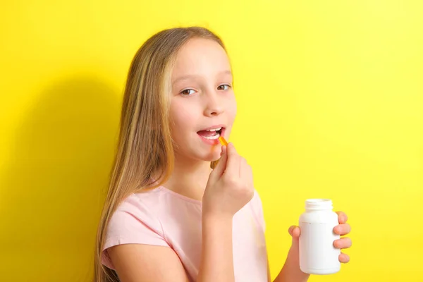 Een tiener meisje houdt een omega 3 capsule in haar handen op een gekleurde achtergrond. — Stockfoto