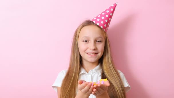 Девочка-подросток в праздничной кепке бросает конфетти на цветном фоне крупным планом — стоковое видео