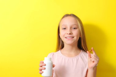 Genç bir kız elinde renkli bir arka planda omega 3 kapsülü tutuyor.. 