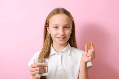 Genç bir kız elinde renkli bir arka planda omega 3 kapsülü tutuyor.. 