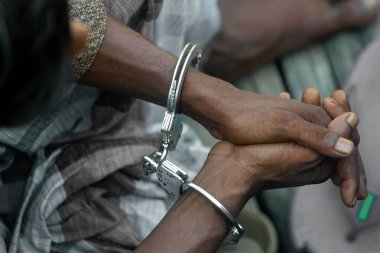 Tutuklanan Asyalı bir suçlu kelepçelendikten sonra oturuyor. Sanık genç bir köy yukarıdan otururken görülüyor. Sanığın ellerinde kelepçe. Bir suçluyu tutukladılar..