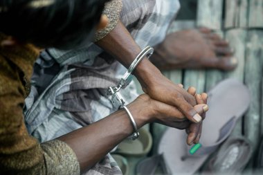 Tutuklanan Asyalı bir suçlu kelepçelendikten sonra oturuyor. Sanık genç bir köy yukarıdan otururken görülüyor. Sanığın ellerinde kelepçe. Bir suçluyu tutukladılar..
