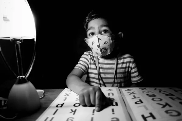 一个戴着安全面具的男孩正坐在家里读一本英文字母学习书 亚洲男孩在灯下学习 儿童教育概念照片 — 图库照片