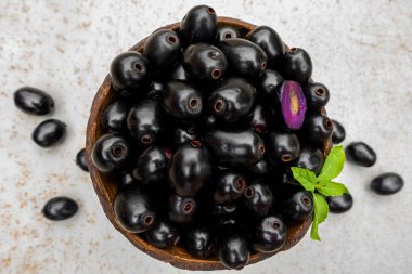 Siyah olgun Syzygium cumini meyveleri. İzole edilmiş beyaz arka planda, ahşap bir kasede koyu siyah kahve eriği. Büyük java eriklerinin üzerinde yeşil nane yaprağı.