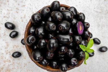 Siyah olgun Syzygium cumini meyveleri. İzole edilmiş beyaz arka planda, ahşap bir kasede koyu siyah kahve eriği. Büyük java eriklerinin üzerinde yeşil nane yaprağı.