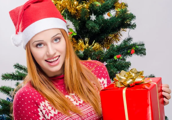 Schöne junge Frau mit Weihnachtsmütze lächelnd mit einem großen Weihnachtsgeschenk. — Stockfoto