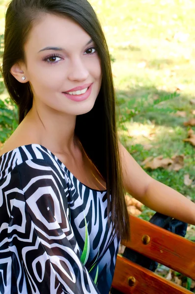 Chica sonriendo sentada en un banco en el parque . —  Fotos de Stock