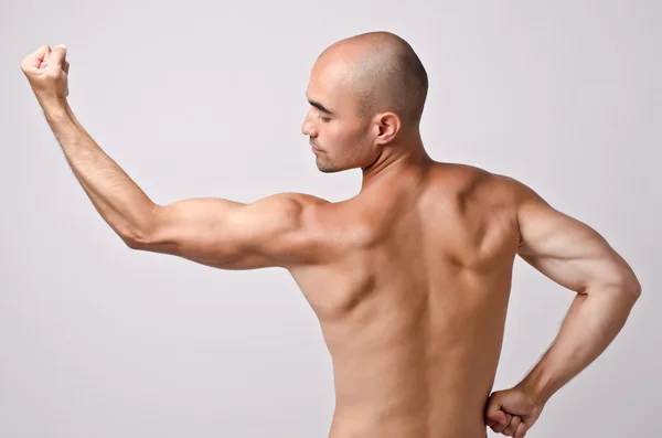 Fit bodybuilder from profile posing with his back flexing his arm showing the biceps. — Stock Photo, Image