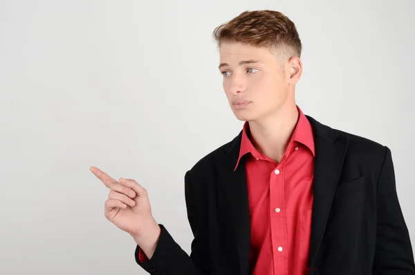 Portrait of a young business man wearing a suit and a red shirt pointing to the side, looking over. — Stock Photo, Image