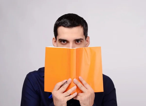 Olhos penetrantes a olhar para um caderno. Estudante segurando um caderno. Professor segurando na frente do rosto um livro com tampa laranja em branco . — Fotografia de Stock