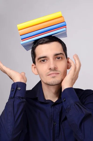 Feliz estudiante sosteniendo un montón de libros en su cabeza. Profesor divertido con libros de colores sobre su cabeza . — Foto de Stock