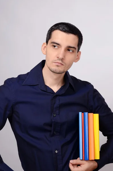 Φοιτητής κρατώντας ένα σωρό βιβλία κάτω από το βραχίονά κοιτώντας μακριά. εκπαιδευτικός με τα πολύχρωμα βιβλία στο χέρι του, ψάχνει την πλευρά. — Φωτογραφία Αρχείου
