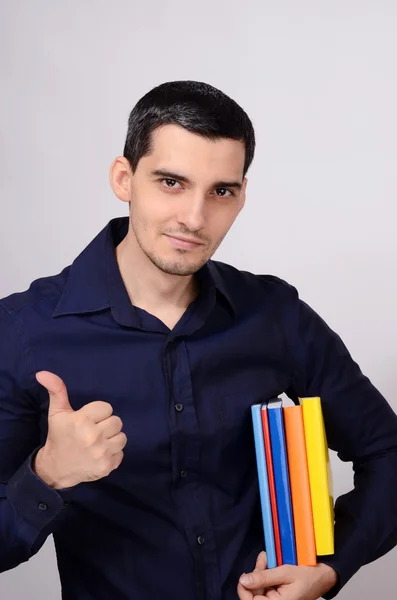 Ein glücklicher Student hält einen Stapel Bücher unter dem Arm und signiert Daumen hoch. Lehrer mit bunten Büchern in der Hand lächelt. — Stockfoto