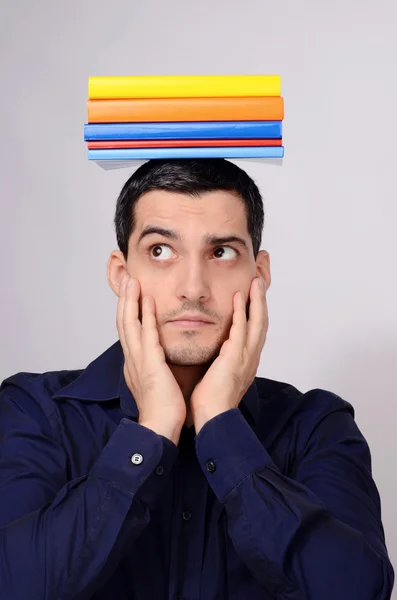 Podejrzane studentów posiadających stos książek na głowę podnosząc jego brwi. śmieszne nauczyciel z kolorowych książek nad głową, patrząc na stronie zastanawiasz się. Obrazek Stockowy