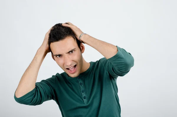 Young man holding his head frowning with worry screaming. Man pulling his hear for worry, sadness, desperation. — Stock Photo, Image