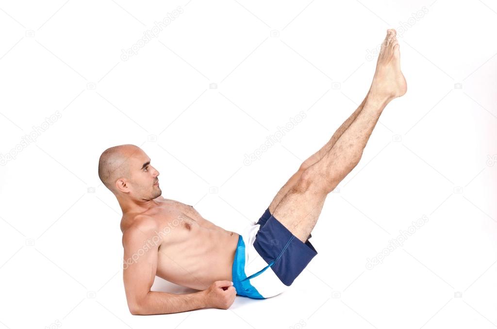 Topless man lying down on the ground doing lower abs exercise by lifting his legs up.