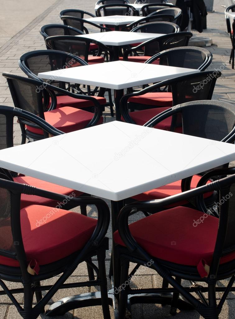 Rows of white empty tables and black wicker chairs in an open air cafeteria.