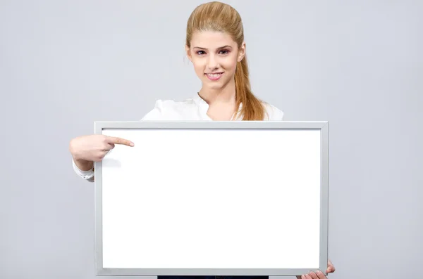 Young girl smiling and pointing to a white blank board. — Stock Photo, Image