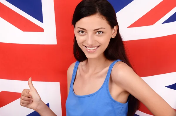 Portrait of a beautiful British girl smiling and signing thumbs up. Young woman standing with the UK flag in the background. — Stock Photo, Image