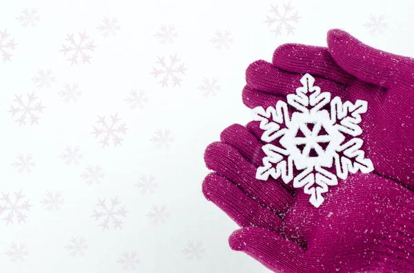 Feche as mãos usando luvas rosa segurando um grande floco de neve. Mitenes e floco de neve em um fundo de neve branco . — Fotografia de Stock