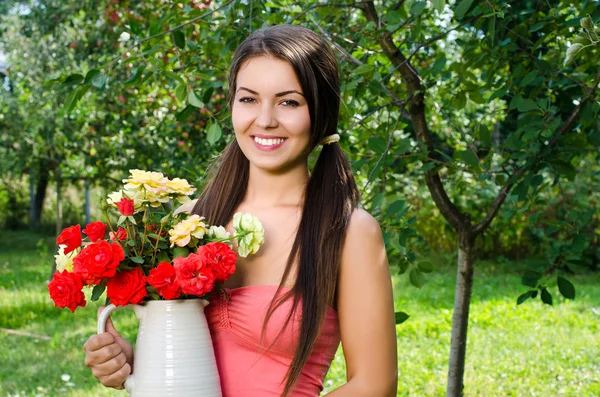 Dívka s úsměvem, drží váza s kyticí červených a žlutých růží v horkém letním dni. — Stock fotografie