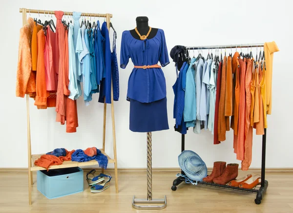 Dressing garderob med kompletterande färger blå och orange kläder ordnade på galgar och en outfit på en skyltdocka. — Stockfoto