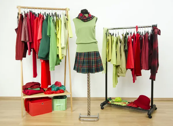 Armário de vestir com cores complementares roupas vermelhas e verdes dispostas em cabides e uma roupa em um manequim . — Fotografia de Stock