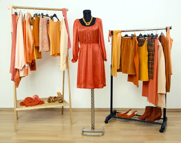 Garderobe met oranje kleding gerangschikt op ruimte voor hangers en een jurk op een mannequin. — Stockfoto