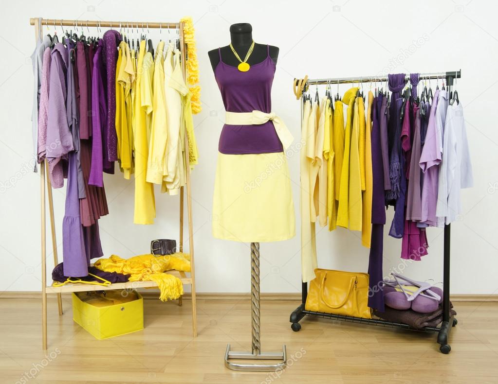 Wardrobe with complementary colors purple and yellow clothes arranged on hangers and an outfit on a mannequin.