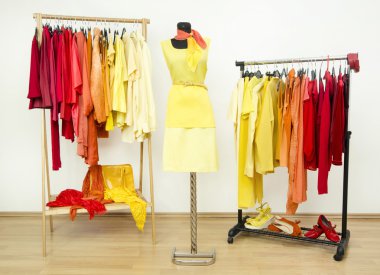 Wardrobe with yellow, orange and red clothes arranged on hangers and a yellow outfit on a mannequin. clipart