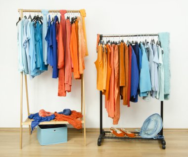 Wardrobe with complementary colors orange and blue clothes hanging on a rack nicely arranged. clipart
