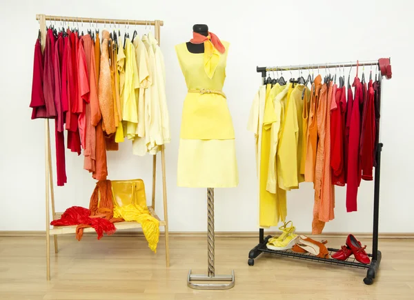 Wardrobe with yellow, orange and red clothes arranged on hangers and a yellow outfit on a mannequin. — Stock Photo, Image