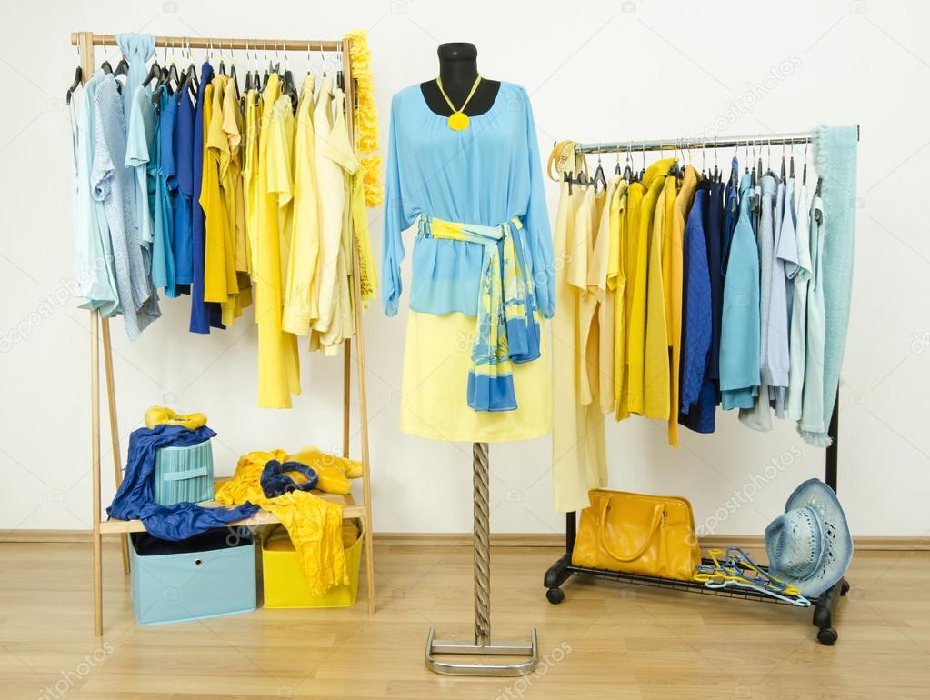 Wardrobe with yellow and blue clothes arranged on hangers and an outfit on a mannequin.
