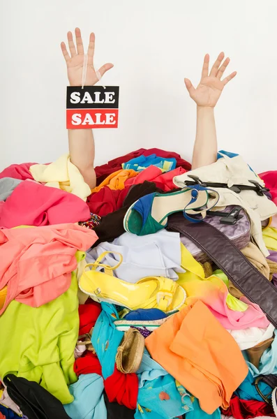 Man hands with the sale sign reaching out from a big pile of clothes and accessories. — Stock Photo, Image