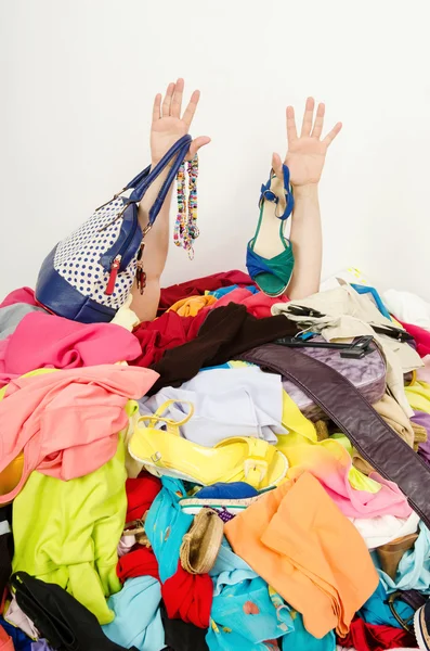 Mãos de homem estendendo-se de uma grande pilha de roupas e acessórios . Imagem De Stock