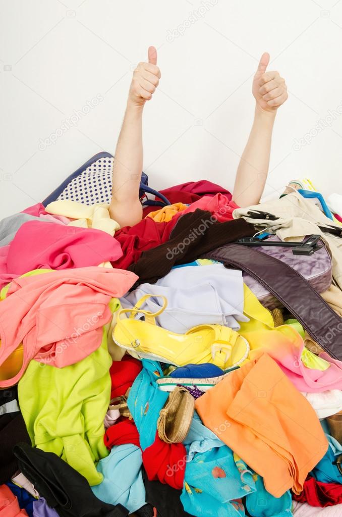 Man hands signing thumbs up reaching out from a big pile of clothes and accessories.