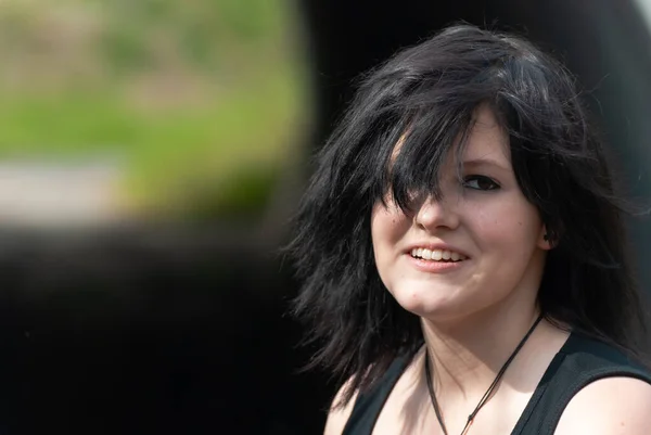 Serseri emo kızı, siyah saçlı ve göz kalemi olan genç bir yetişkin, gülümseyen, kameraya bakan, açık havada, yatay, yakın plan