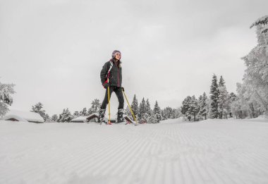 Kahverengi saçlı, kayak kıyafeti giyen, dağın tepesinden kayak yaptıktan sonra vadide duran, alçak açılı, yatay manzaralı bir kadın.