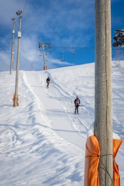 Kayaklı bir kadın, snowboard 'lu bir adam siyah spor giysiler giyiyor, kayak kaldıracı kullanıyor, dağın tepesine çıkıyor, dikey, dikey.