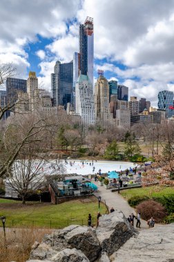 Wollman Pink ile gündüz vakti buz pateni, uzaktan görüş, Central Park New York Şehri, banklar ve önde yürüyen insanlar, ön tarafta kayalar,