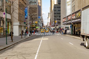 New York City caddesi, Radio City Music Hall 'un yanında. Trafik, sarı taksi ve arabalar. Ufukta iki yaya geçidinin arkasında.