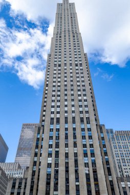 Rockefeller Center bina cephesi, New York, gündüz görüş açısı düşük, mavi gökyüzü ve bazı bulutlar, binanın camlarında yansıma, dikey.