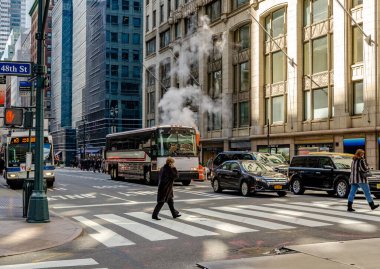 Manhattan 'da yaya geçidinde 48. Cadde' de insanlar arka planda bekleyen arabalar ve iki otobüs, New York 'ta gündüz vakti bir otobüsün arkasında dumanlar yükseliyor.