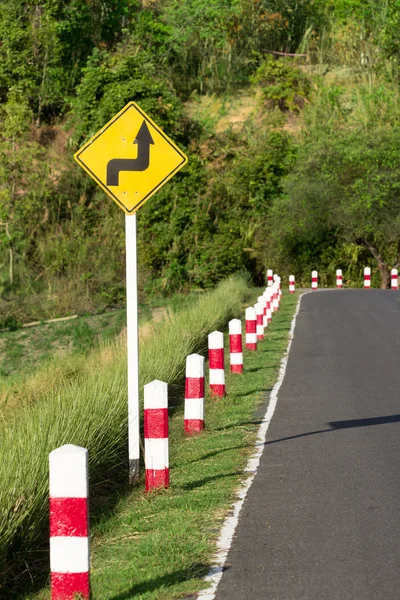 Um sinal de estrada avisa de uma curva acentuada em uma estrada estreita — Fotografia de Stock