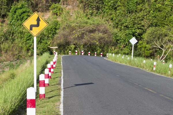 Um sinal de estrada avisa de uma curva acentuada em uma estrada estreita — Fotografia de Stock